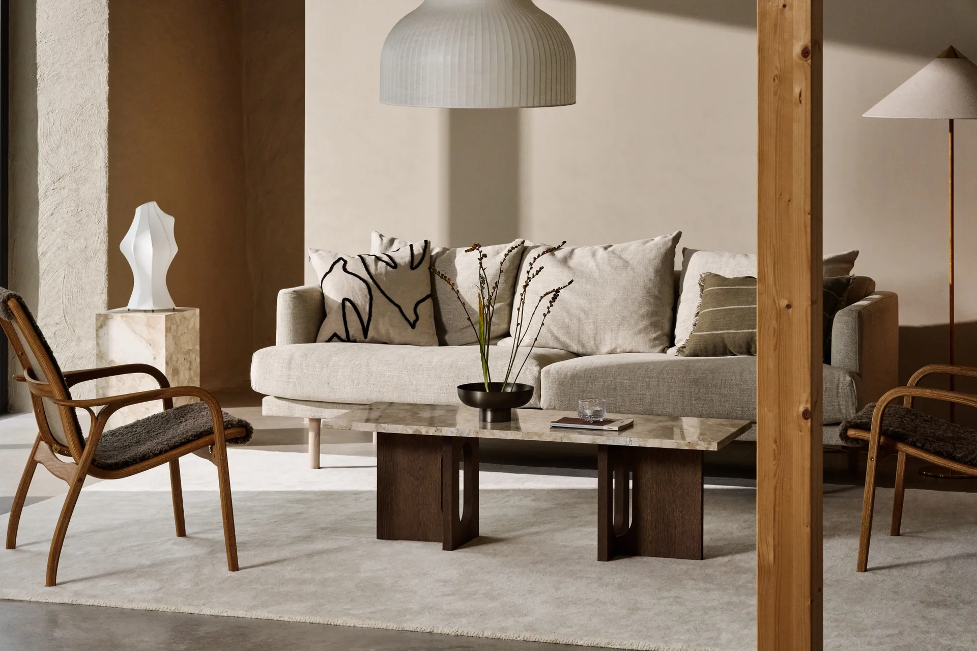 A cozy living room with a light beige sofa, marble coffee table, wood armchairs, and a ribbed pendant lamp.