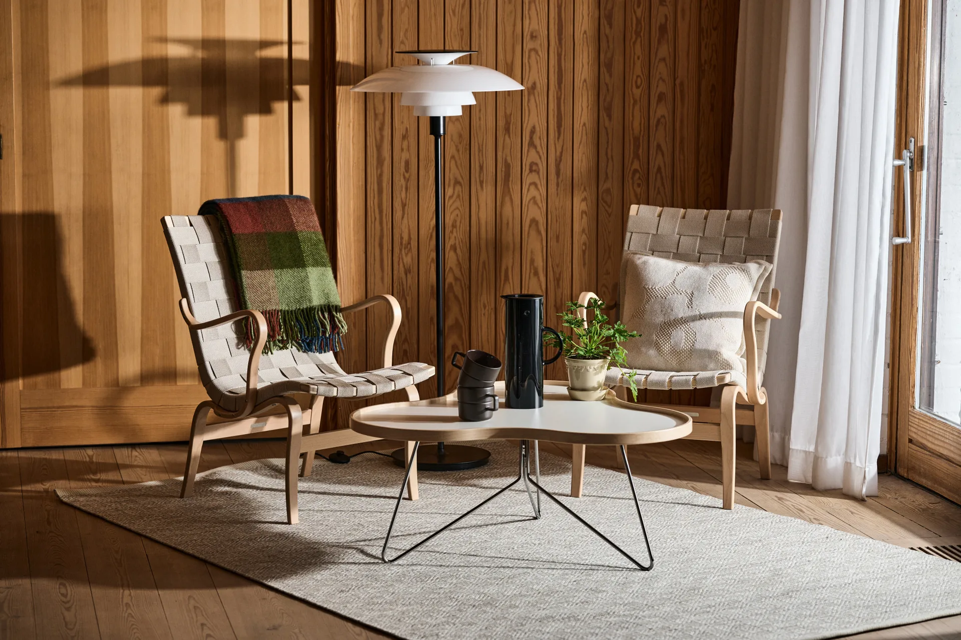 Two light wood chairs with woven seats, a white coffee table, and a tiered floor lamp in a cozy room with wood paneling.