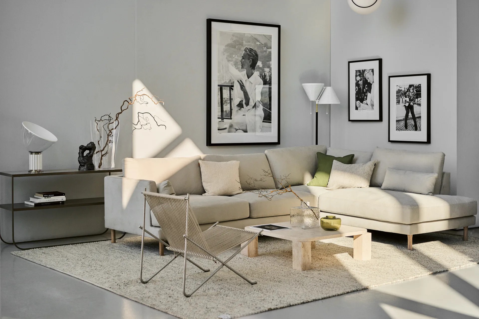 A modern living room with a light beige sectional sofa, a woven chair, a light textured rug, and framed artwork.