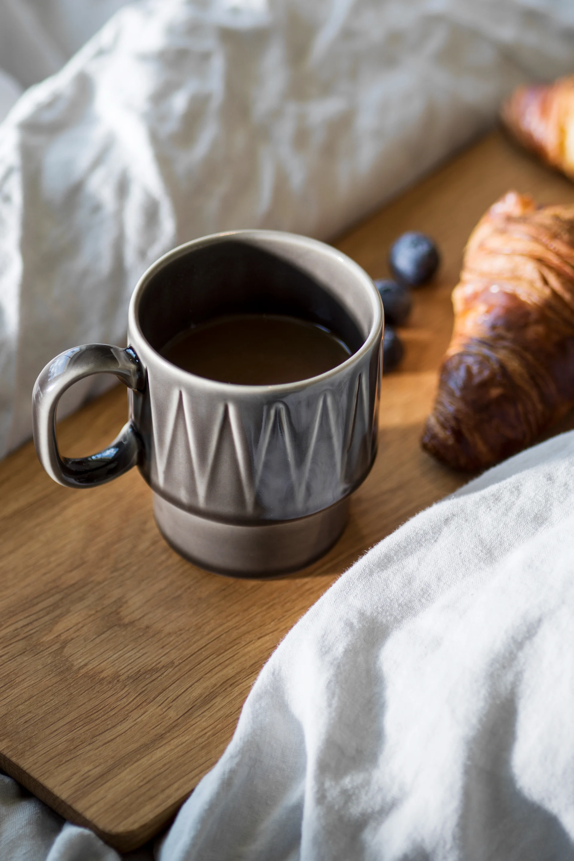 The Coffee & More espresso cup in grey stands on a wooden board in a bed, with a croissant next to it.