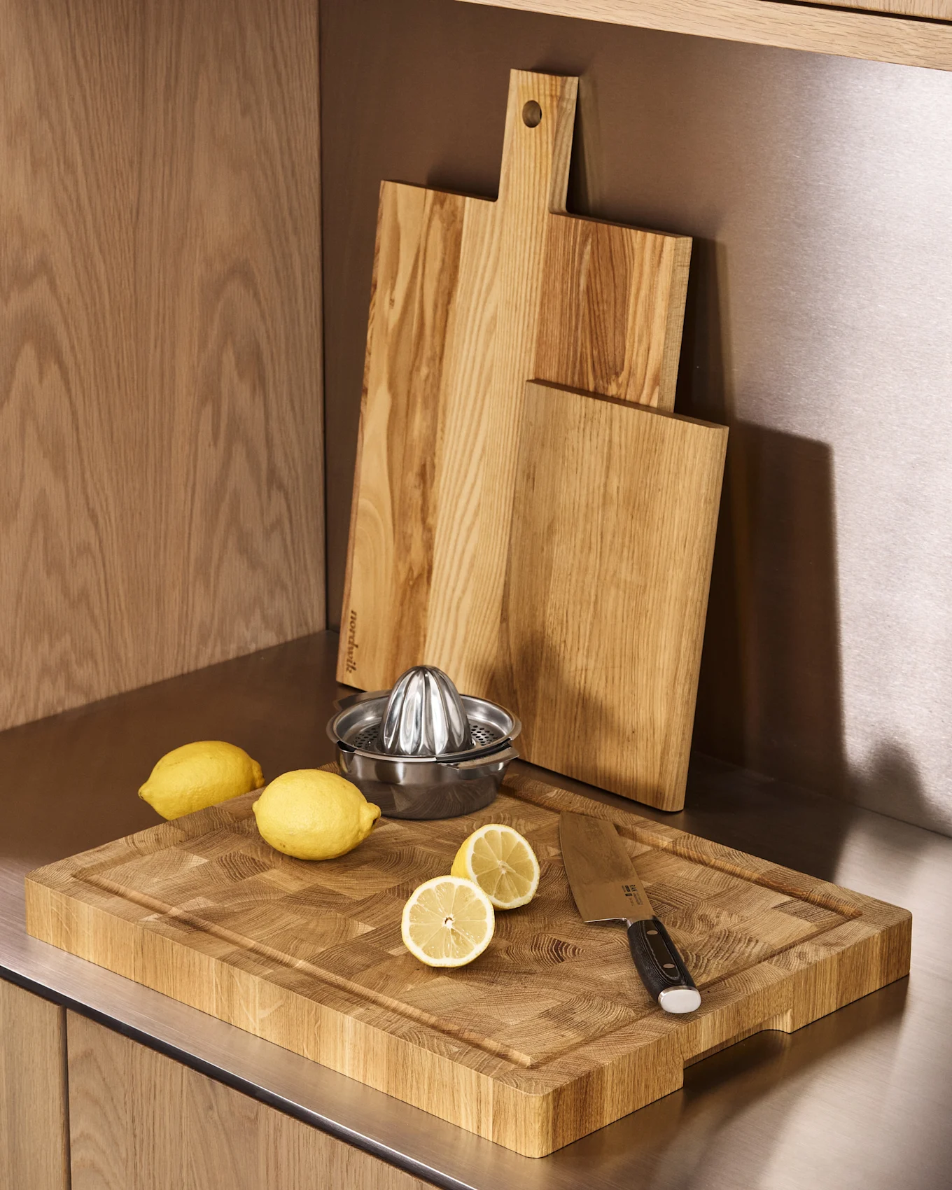 Three wooden cutting boards, a stainless steel citrus juicer, whole and halved lemons on a kitchen counter.