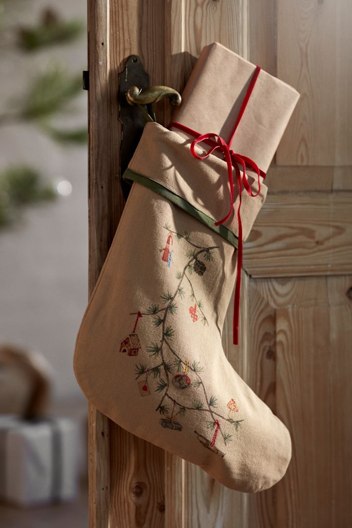 Christmas decorations for 2025 are inspired by nature like this stocking from Kähler that you see here hanging on a wooden door in front of a Christmas tree and wrapped gifts. 
