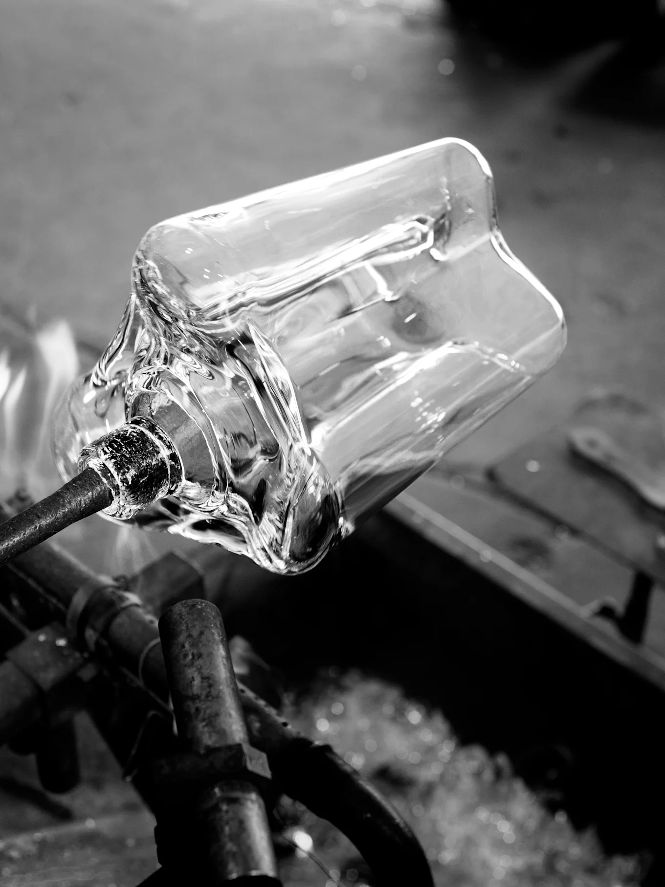 Clear glass vessel being shaped on a metal rod with heat, black and white.
