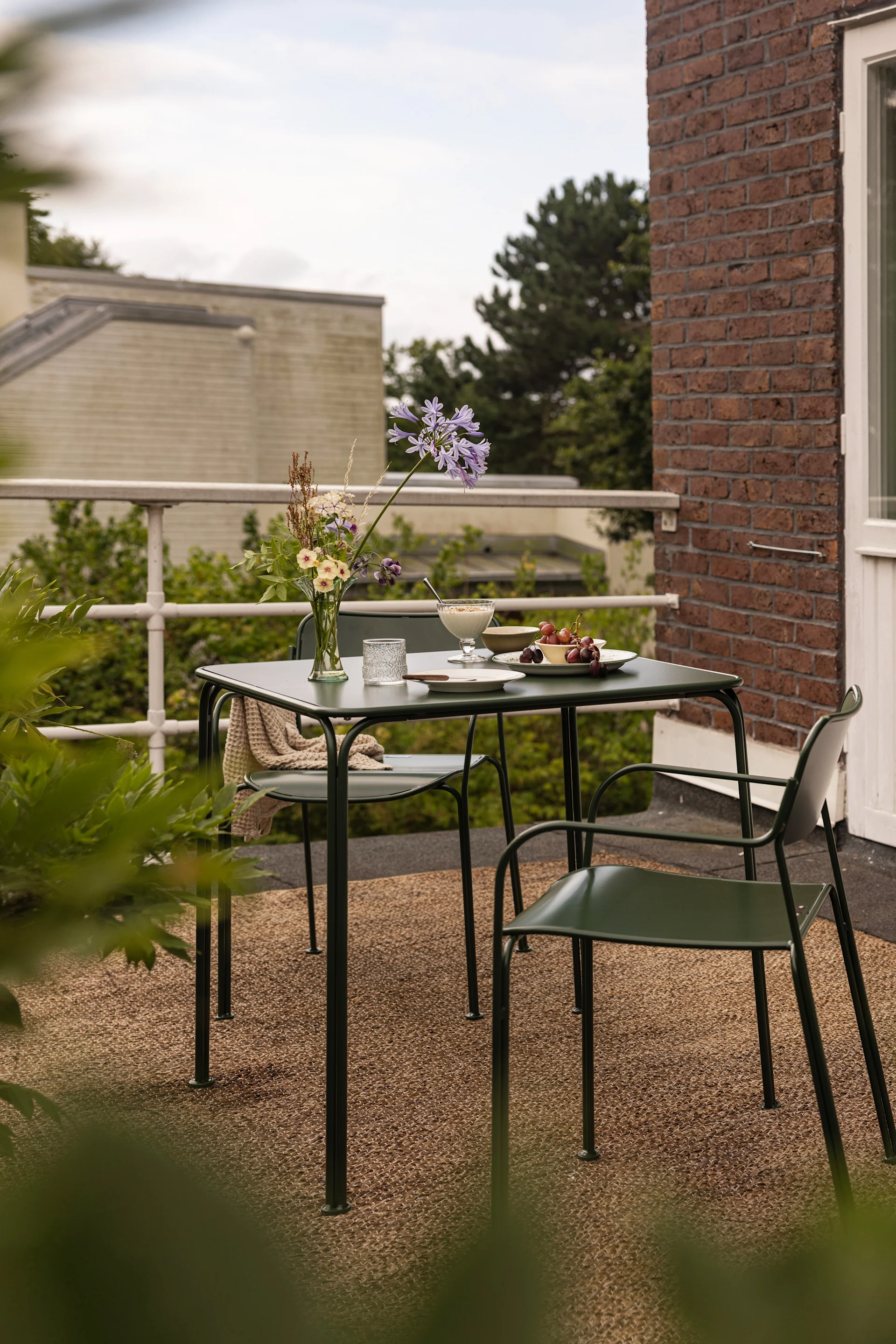 A table and two chairs from the Libelle collection by Grythyttan stand on a balcony.