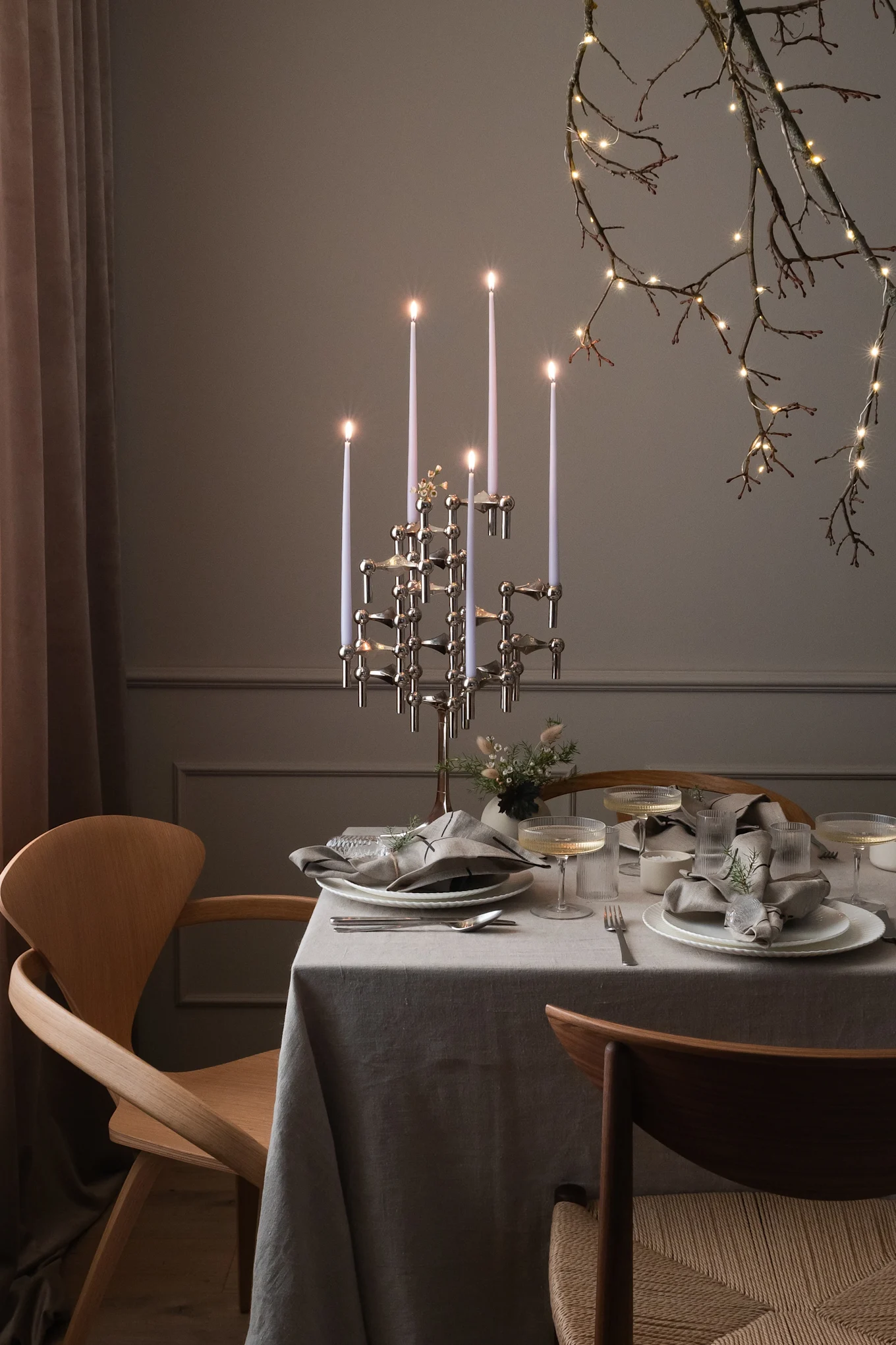 A dining table set for a special occasion with a modern candelabra, place settings, and illuminated branches.