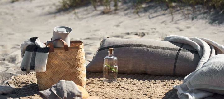 Enjoy a picnic on the beach with these summer essentials, a woven basket from oyoy, a cosy beige picnic blanket from Klippan Yllefabrik and comforting pillows from Ferm Living. 