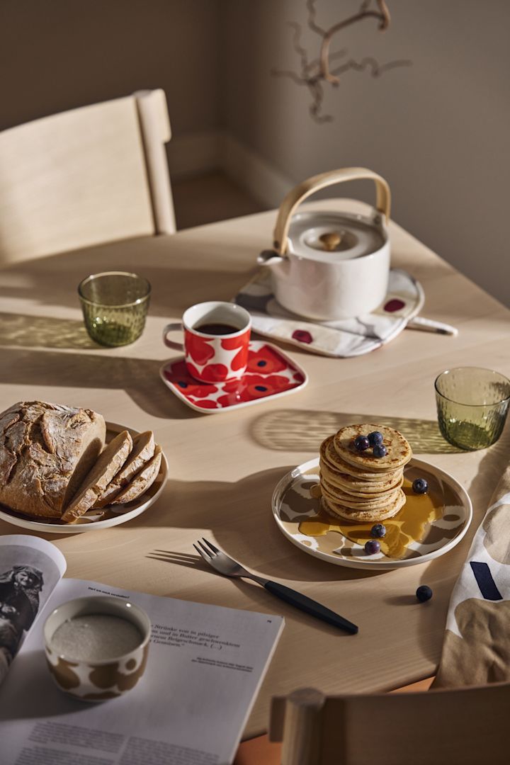 A breakfast table set with the Marimekko Unikko plates and teapot and a stack of pancakes with syrup. 