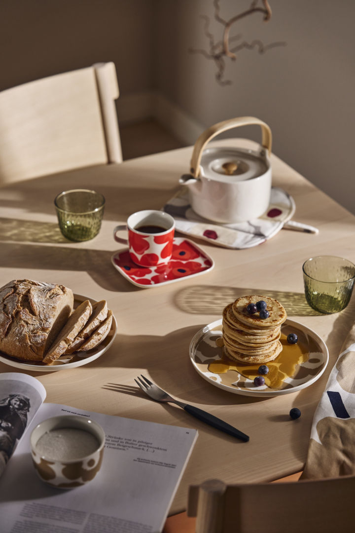 A breakfast table set with the Marimekko Unikko plates and teapot and a stack of pancakes with syrup. 