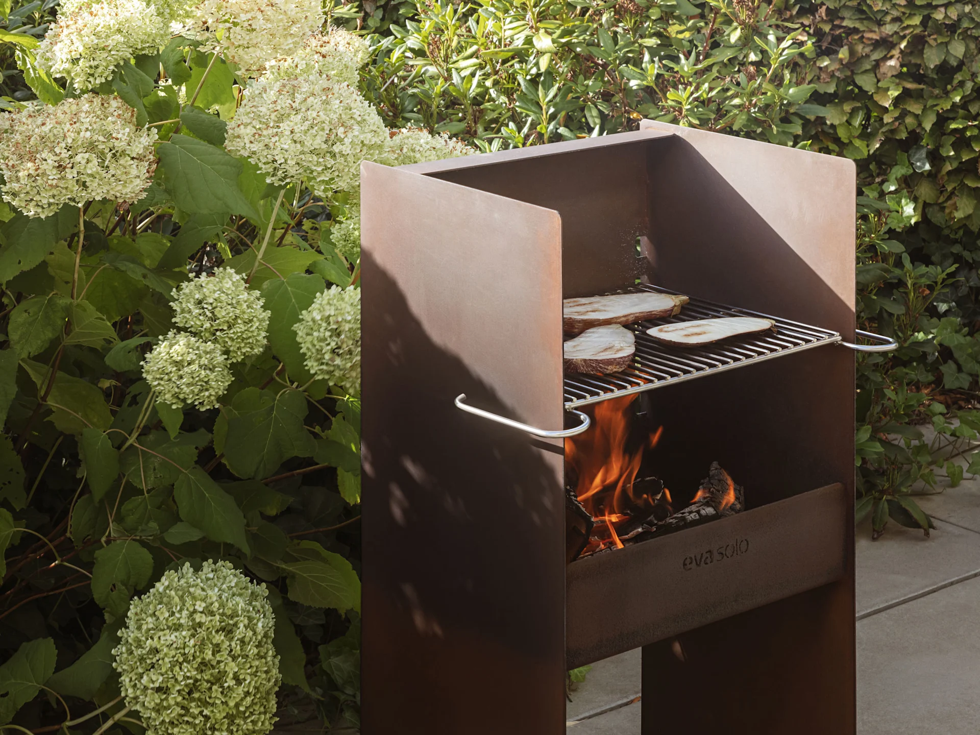 A rustic metal outdoor grill with flames and eggplant slices cooking on the grate.