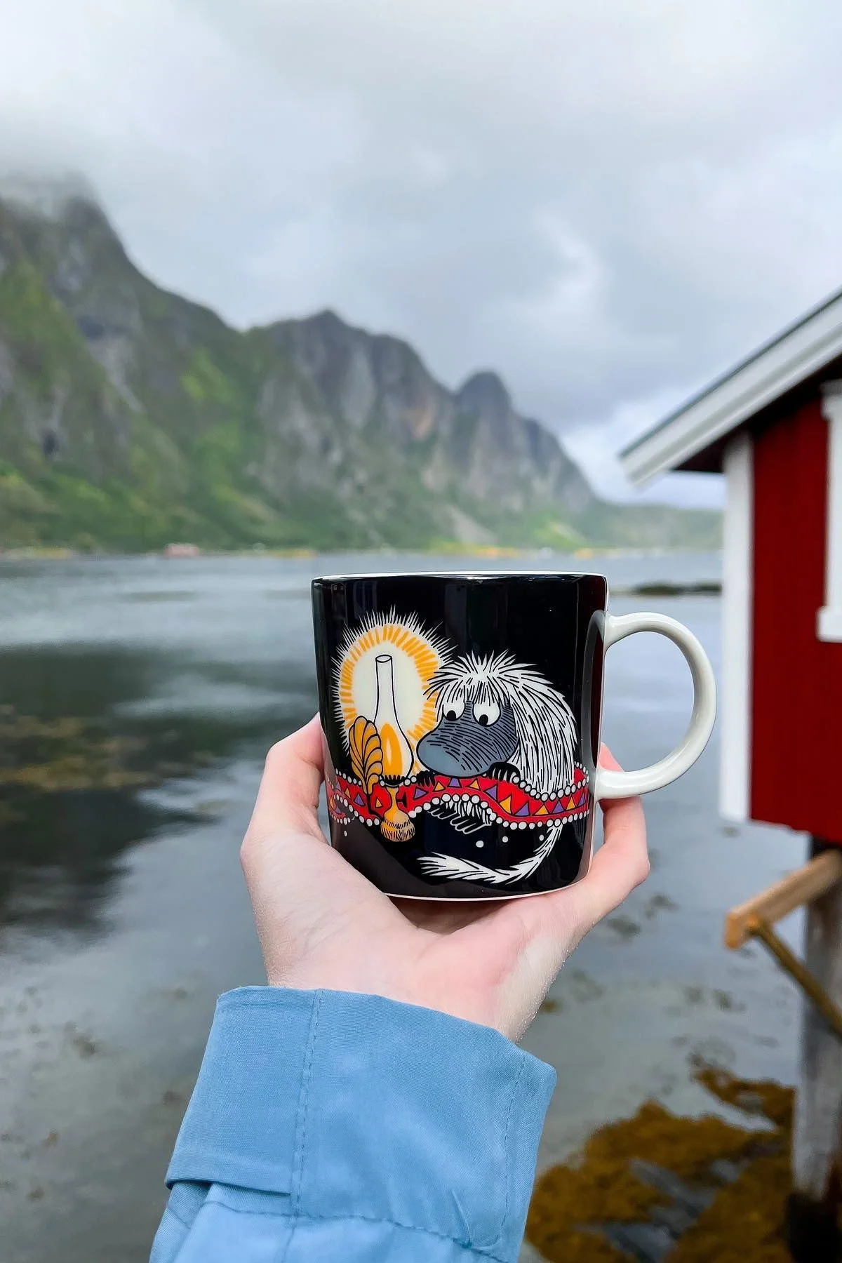 @moominbyingri holds the Urahn moomin cup in her hand, with a rugged Norwegian landscape in the background.