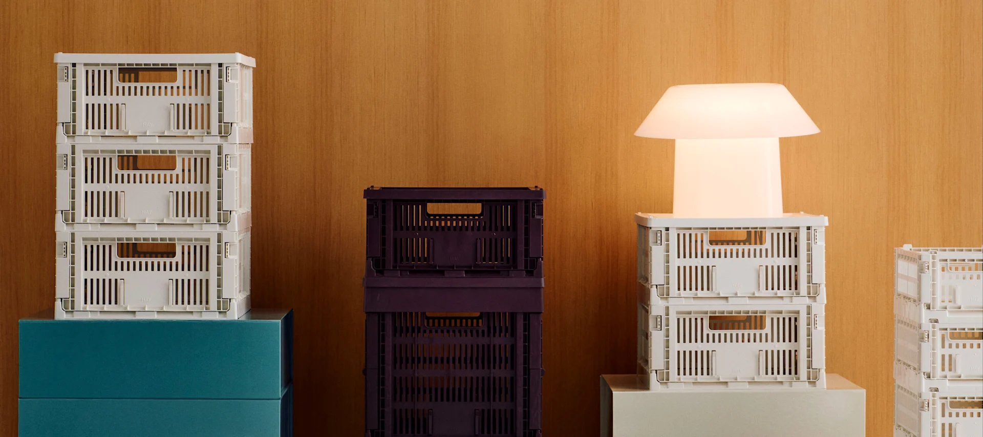 Stacks of white and dark purple collapsible crates with a glowing white modern lamp on a wooden background.