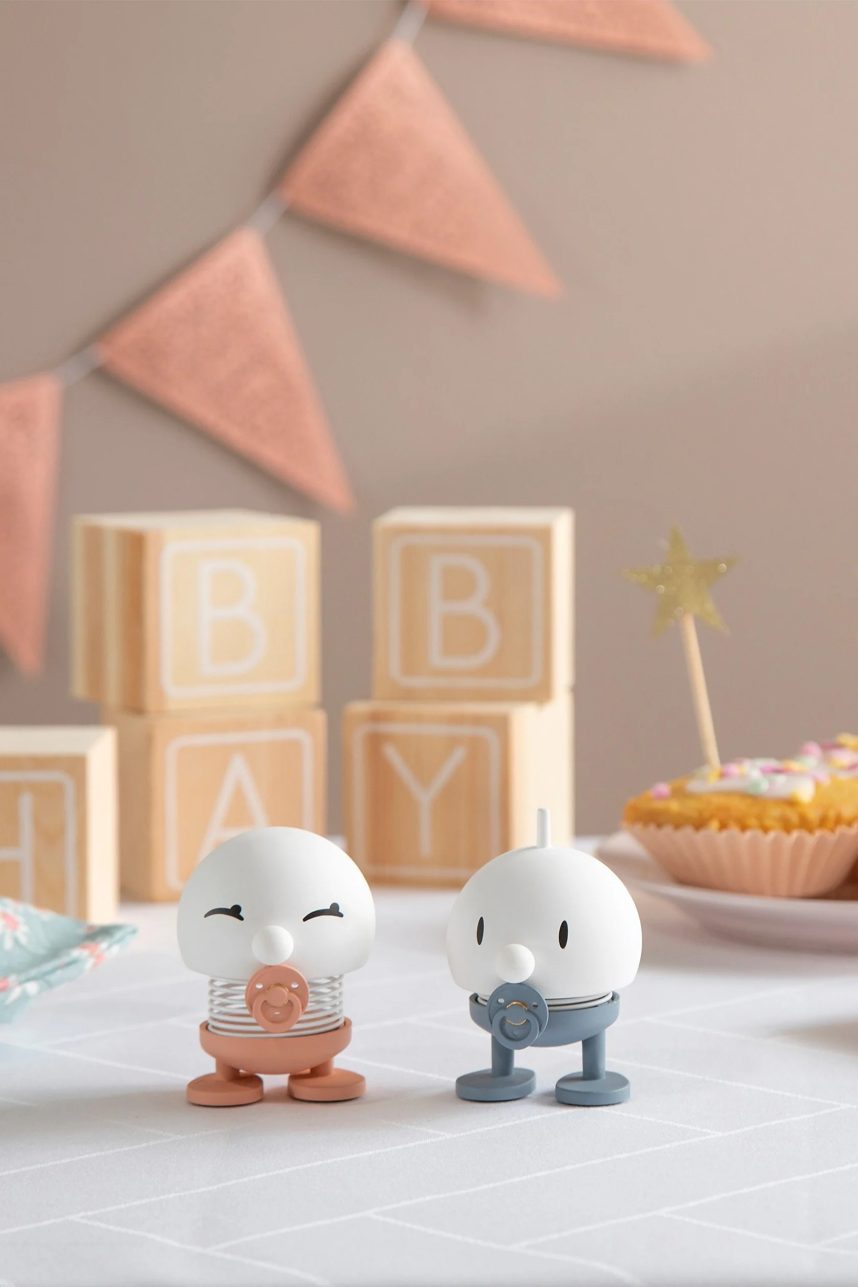 The Hoptimist Baby Bimble is available in pink and blue and stands on a table decorated with presents, garlands and cupcakes.