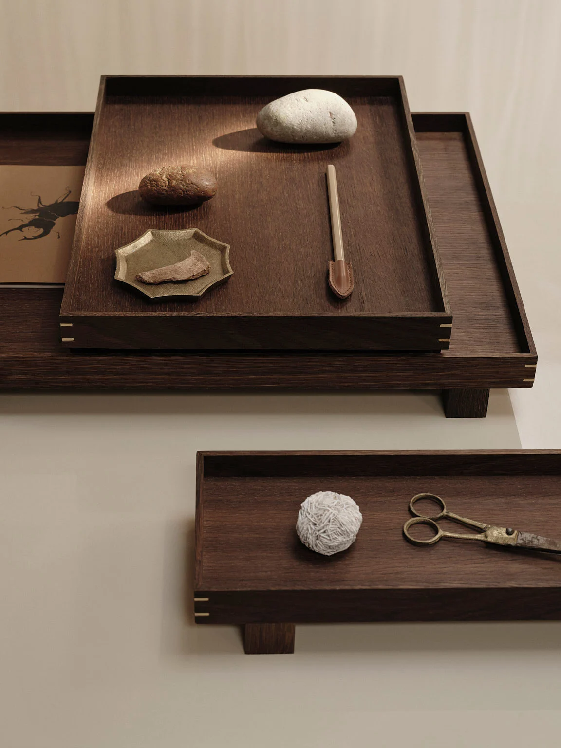 Two dark wooden trays holding natural elements like pebbles, a fibrous ball, antique scissors, and a scoop tool.