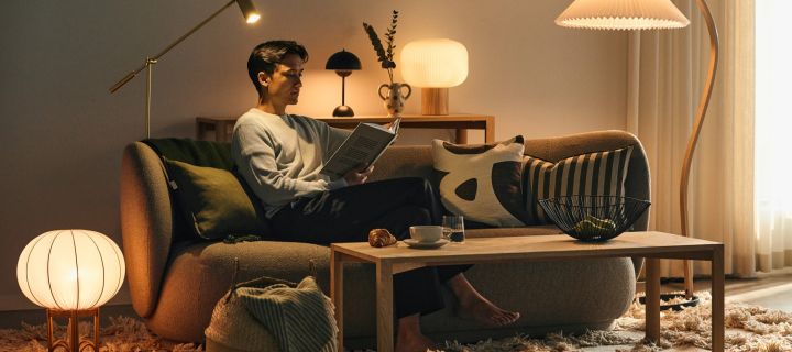 Choosing the right light bulb is important for the feeling in your home - a man sitting on a sofa surrounded by different light sources, reading a book. 