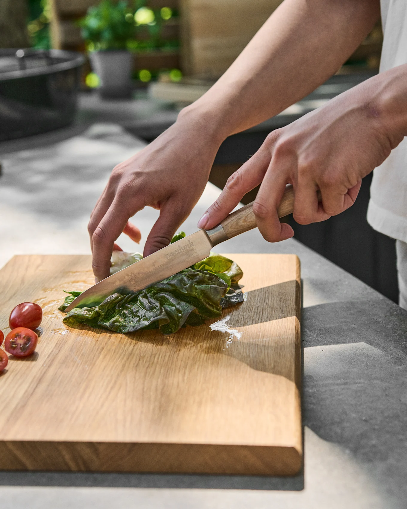 Hands slicing green lettuce on a wooden cutting board next to cherry tomatoes.