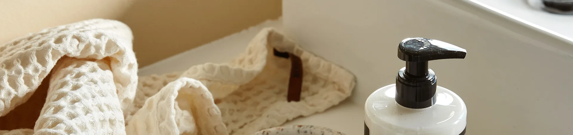 A light-colored, waffle-weave towel folded next to a white pump bottle on a clean, light surface.