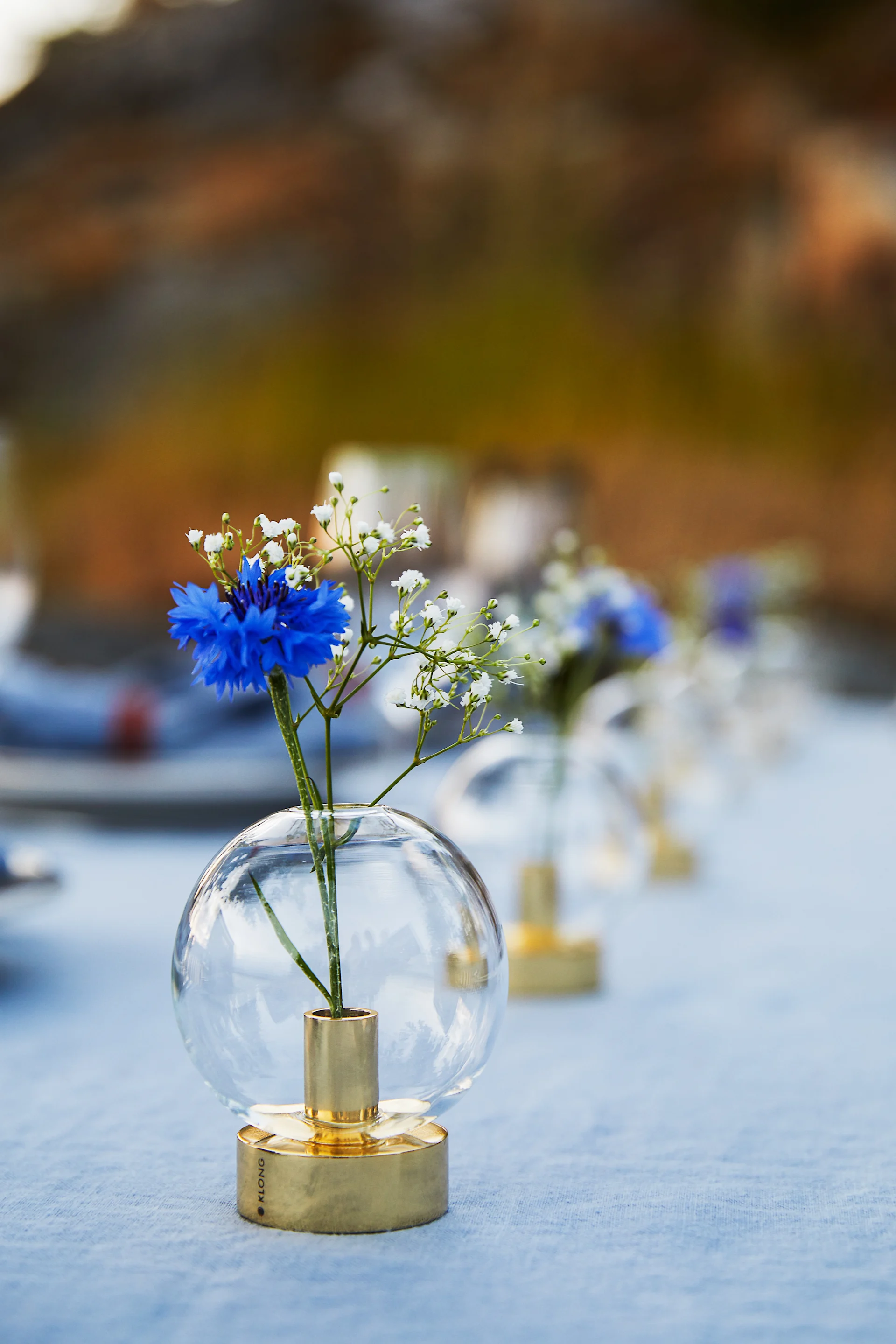 The Orbis vase from Klong stands on an outdoor table, decorated with blue and white flowers and ready for a Swedish crayfish party.