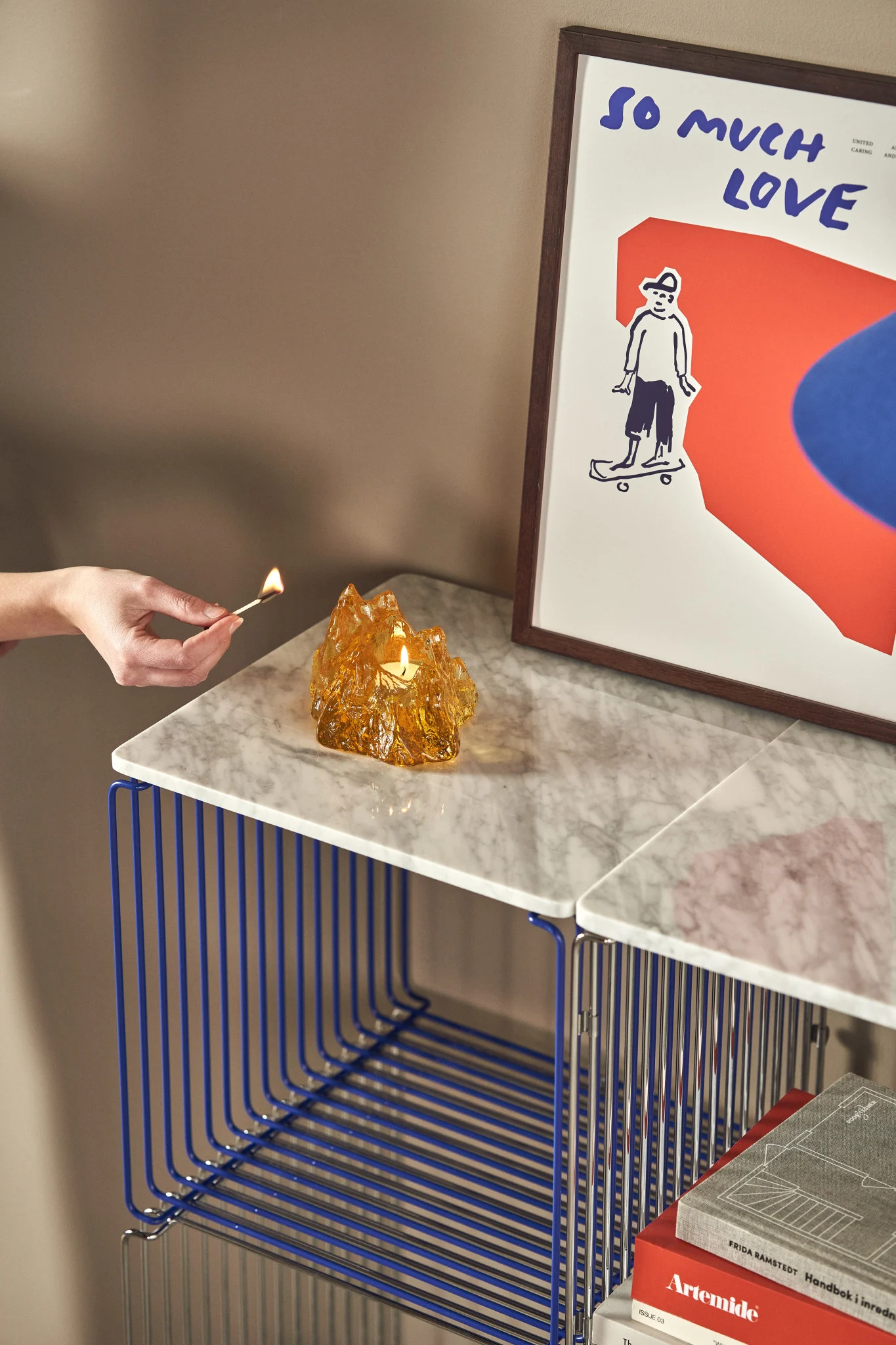 On a Panton Wire shelf stands a yellow The Rock candle holder with a tea light inside that has just been lit.