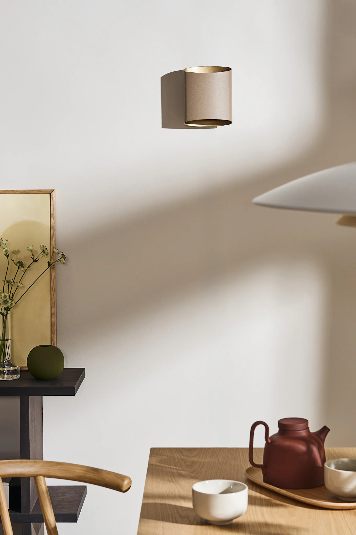 Layer your dining room lighting ideas like the Sinne wall lamp from Belid seen here in beige on the wall of a dining room.