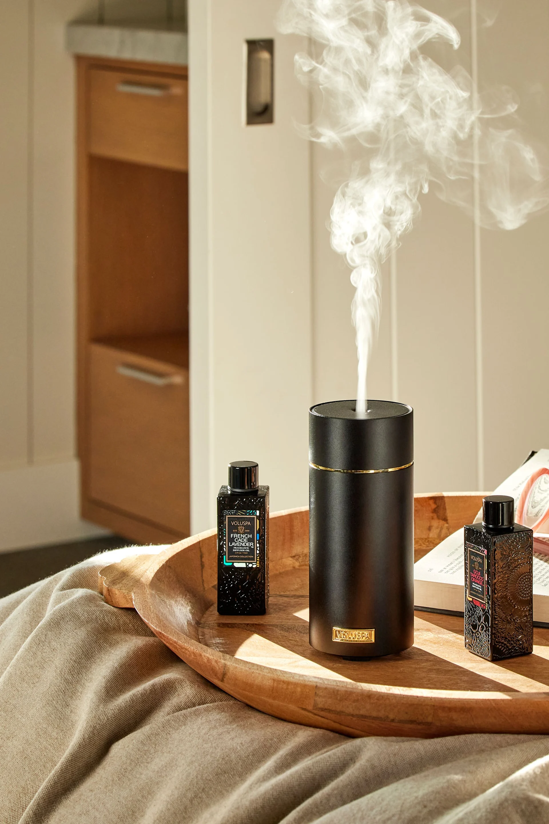 The grey stone diffuser from Volant stands on a pile of books in front of a mirror, with a plant next to it. Give it as a gift for Mother's Day to create a spa feeling.