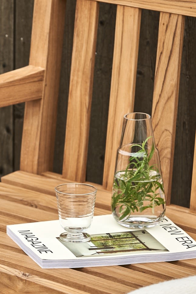 The Viva carafe, filled with rosemary and water stands with the matching glass on an outdoor bench