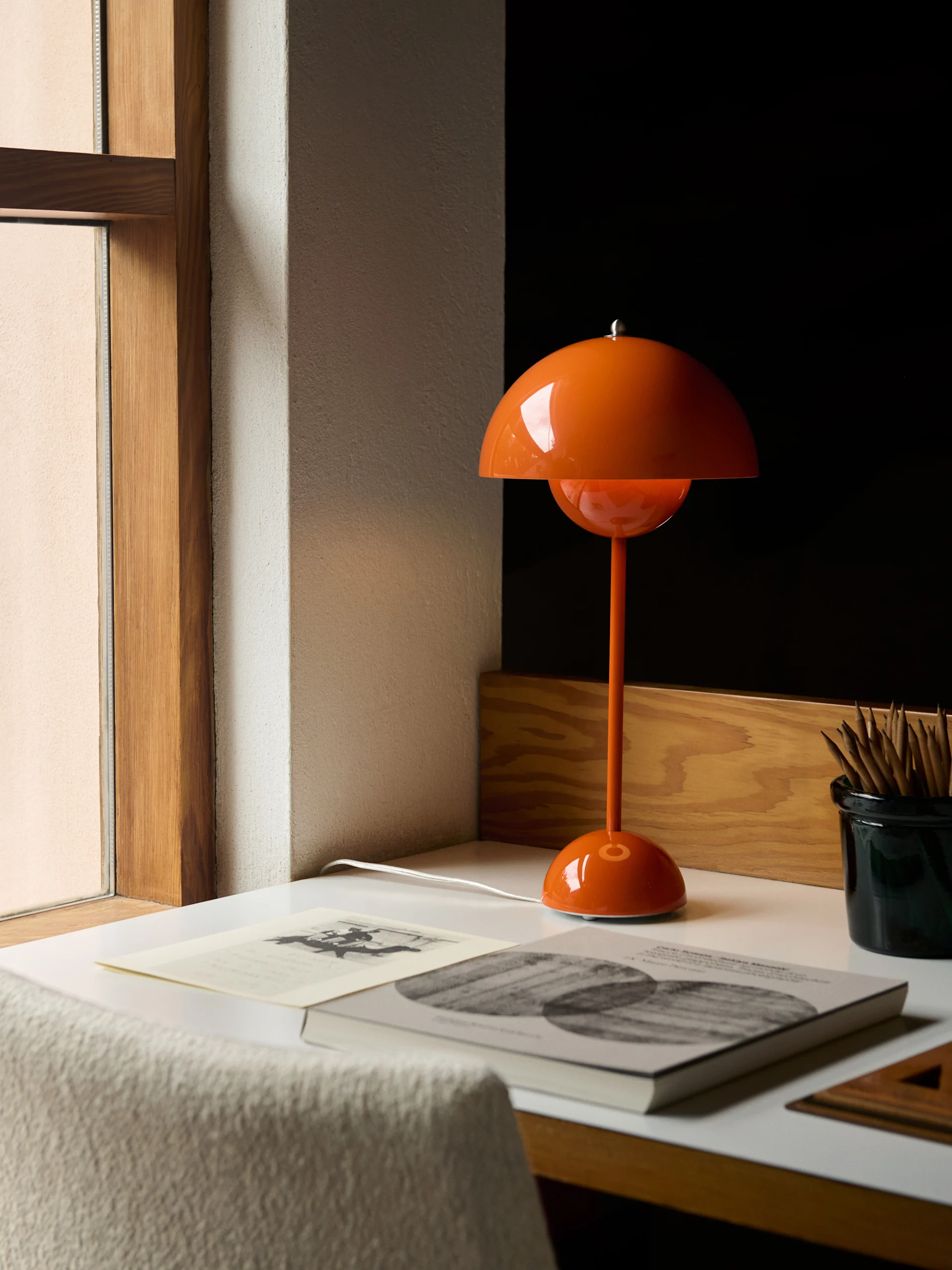 An orange domed table lamp sits on a white desk next to books and a container of pencils.