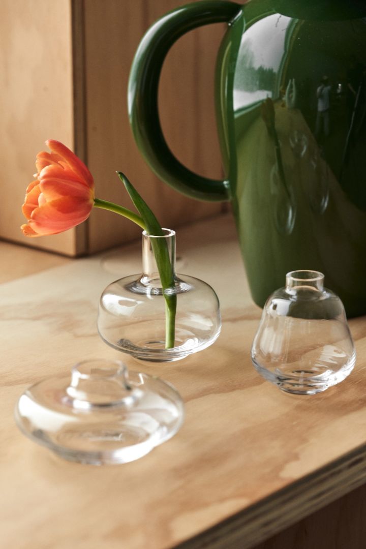 Three mini vases from Kosta Boda stand on a windowsill, one with a fresh red flower.