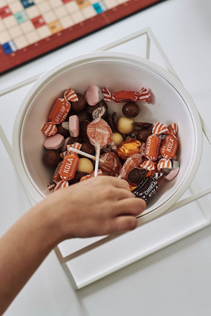 A hand picks out a piece of candy from the white Kubus bowl from Audo Copenhagen.