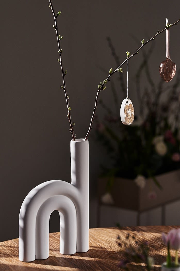 White and trendy Rope vase from DBKD filled with branches for easter with stylish easter decorations hanging in them.