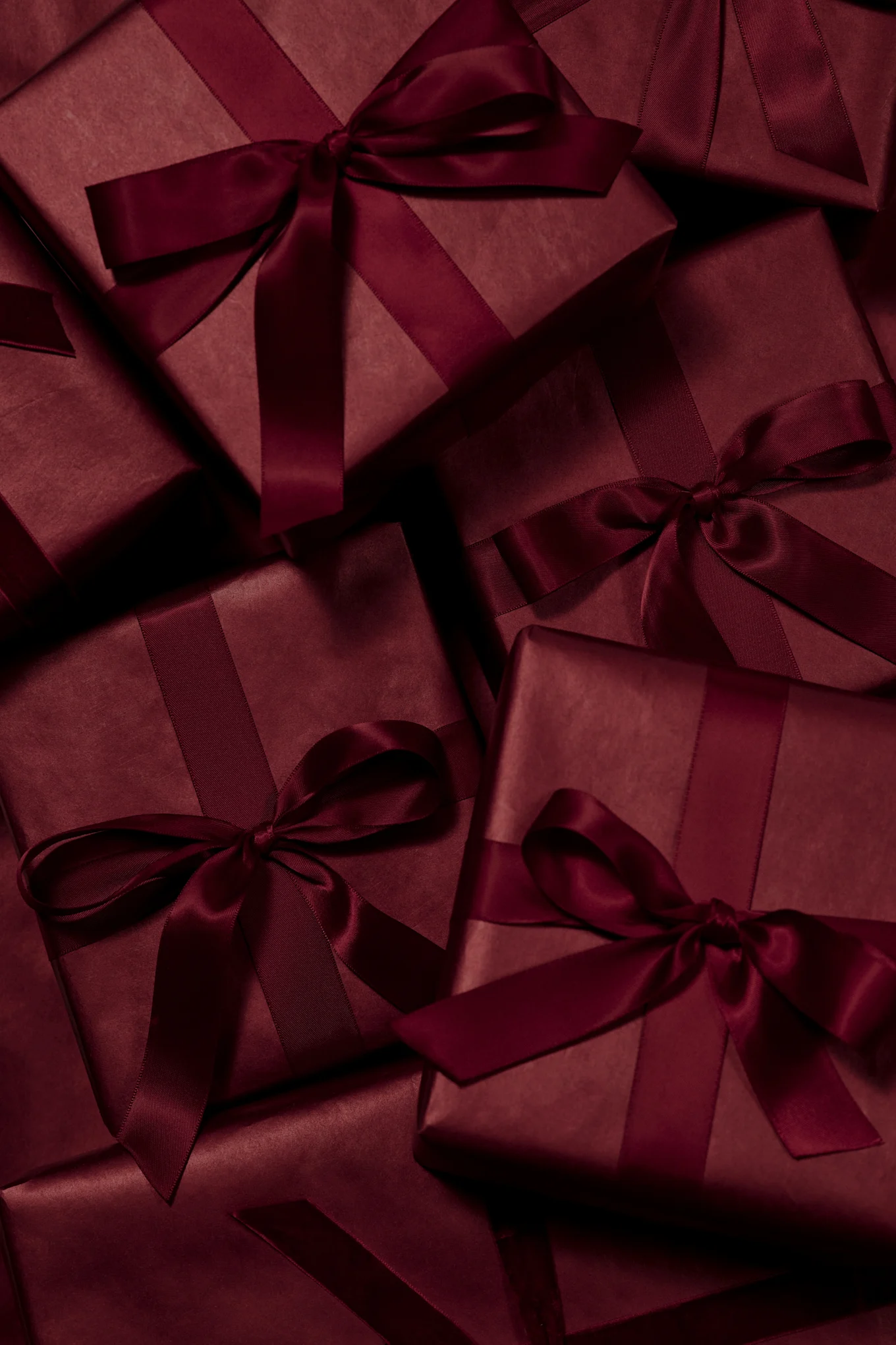Multiple dark red gift boxes wrapped with matching satin ribbons and bows.