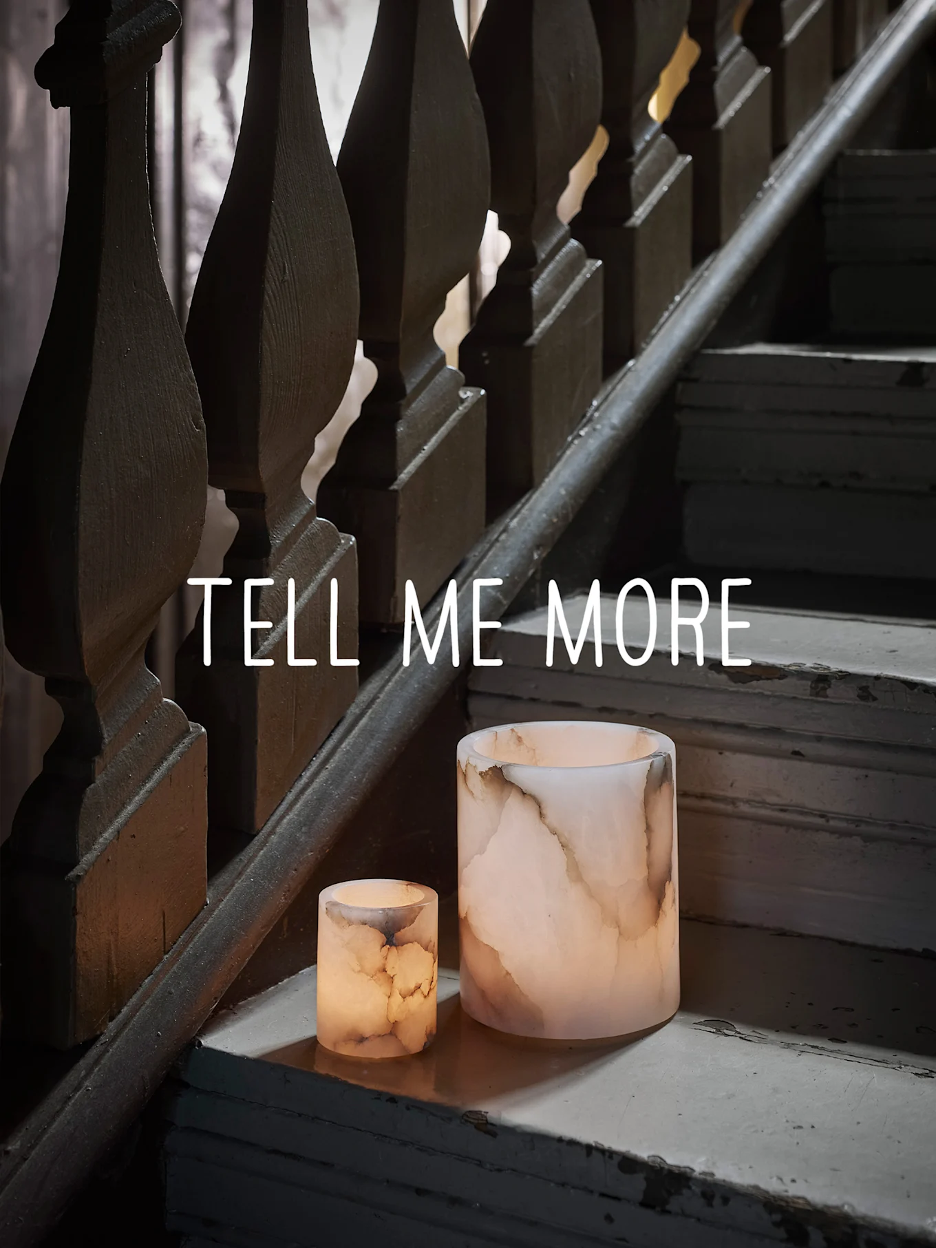 Two glowing onyx-like candle holders on a worn wooden staircase, with "TELL ME MORE" text.