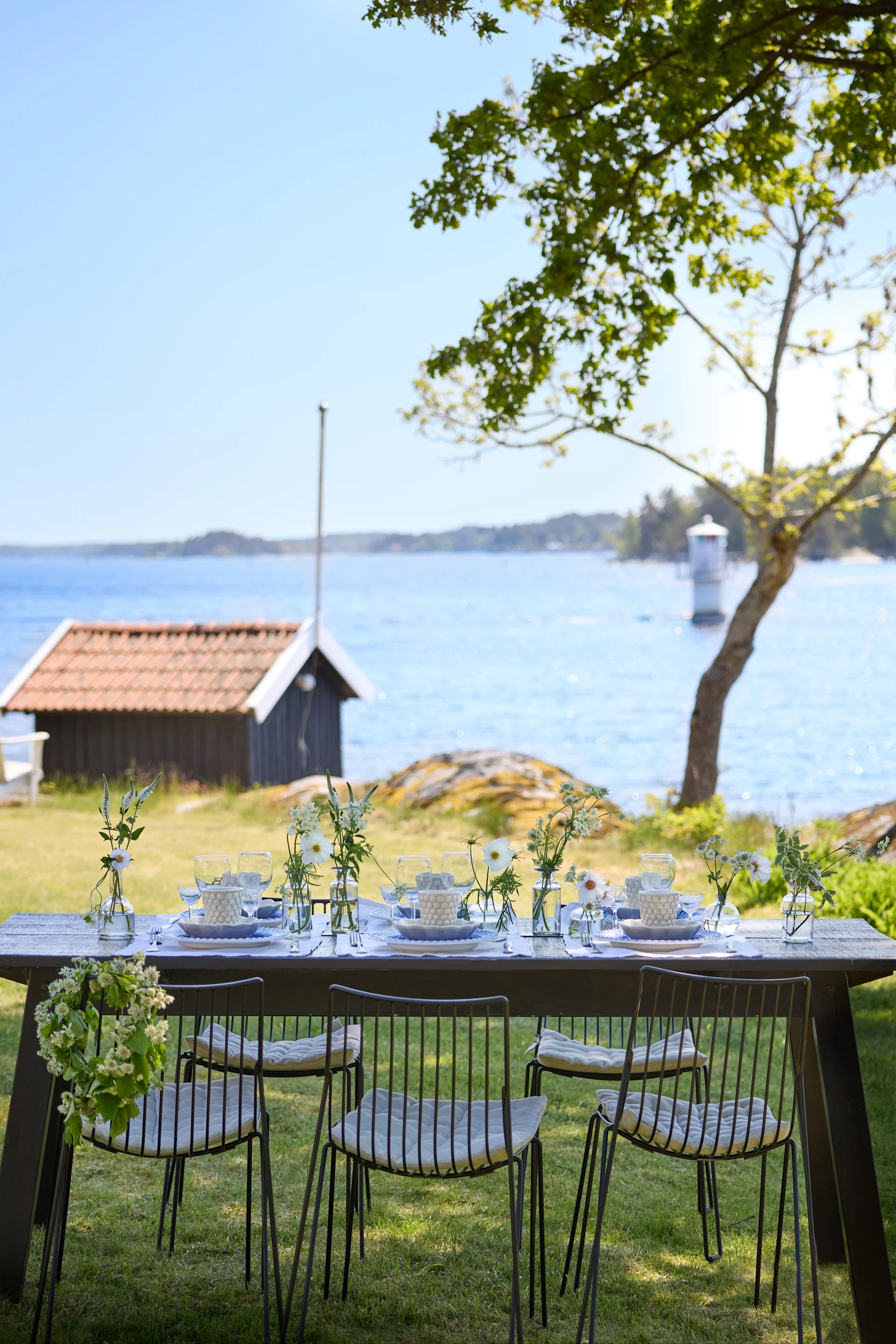 A table set with Mateus crockery in blue and white in a green setting with a view of a small house and a lake.