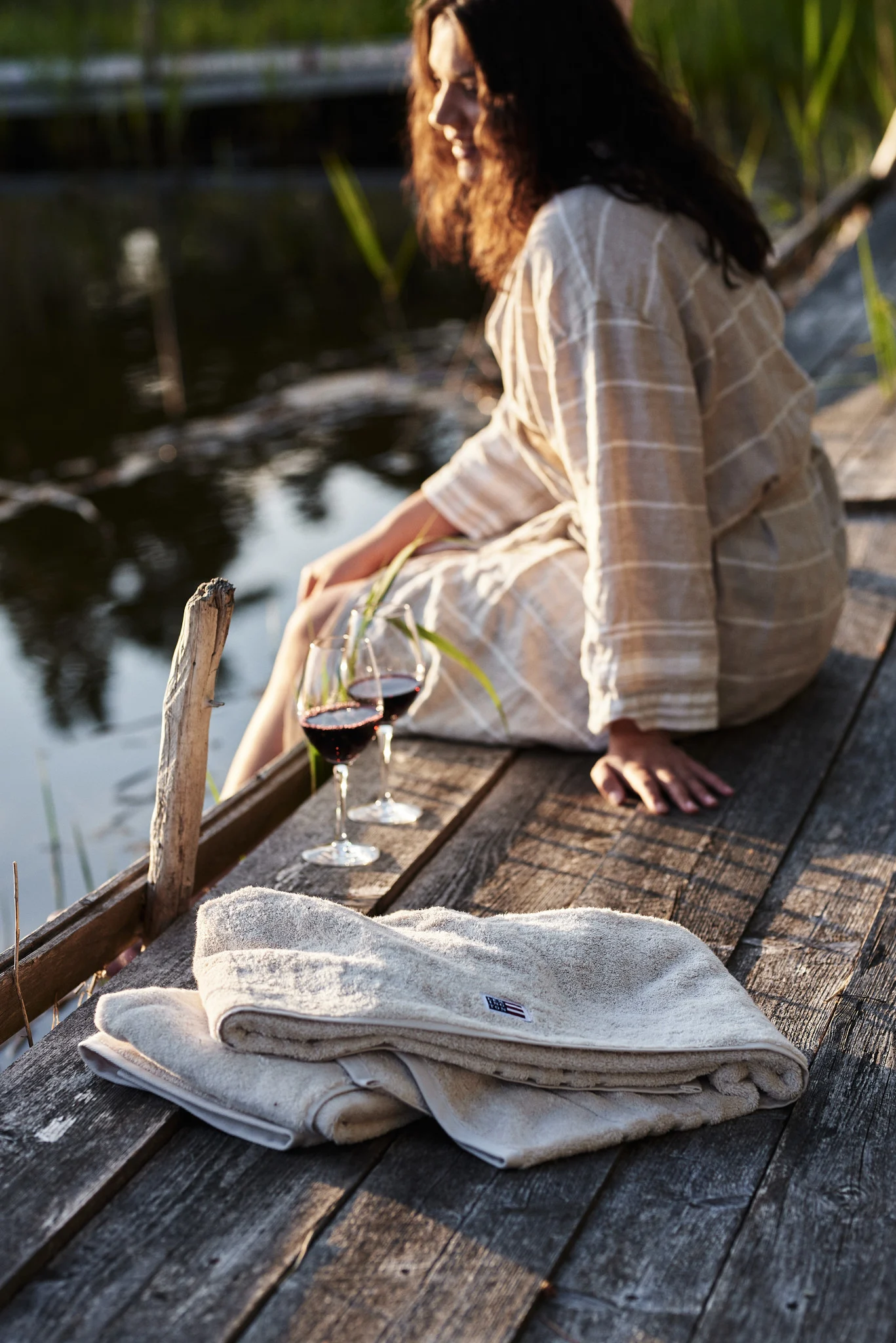 A woman sits on a jetty next to two glasses of wine after an evening swim. A must on any Swedish summer bucket list. 