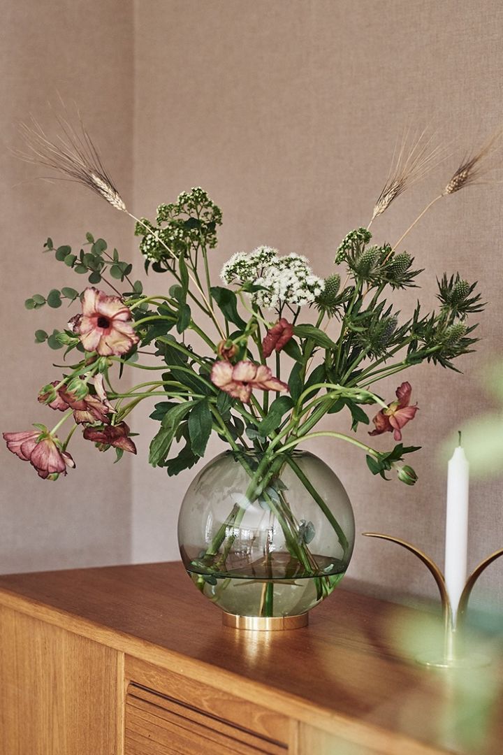 A round vase in a shade of green coloured glass. This round vase is from AYTM and holds a bunch of flowers from Blombruket. 