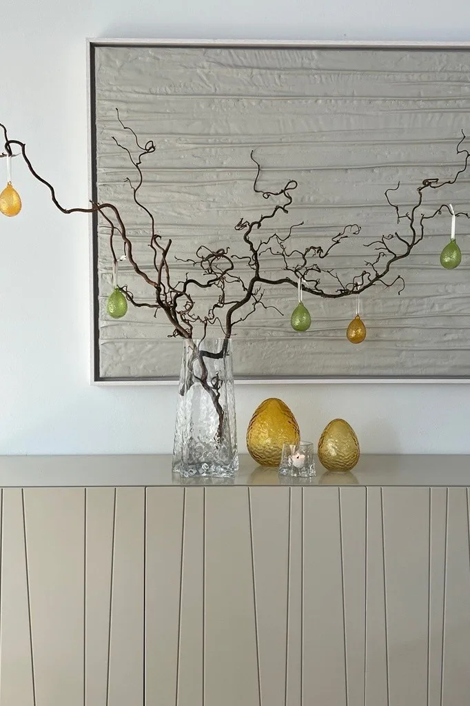 An Easter bush stands on a chest of drawers in the Gry vase, decorated with Gry Easter pendants, next to Gry glass eggs, all from Cooee Design.