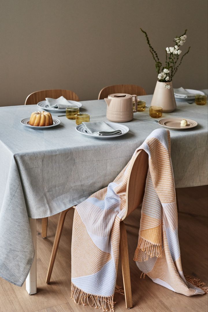 The NJRD Stripes cotton throw in pale yellow and pastel blue draped over a chair at a dining table.