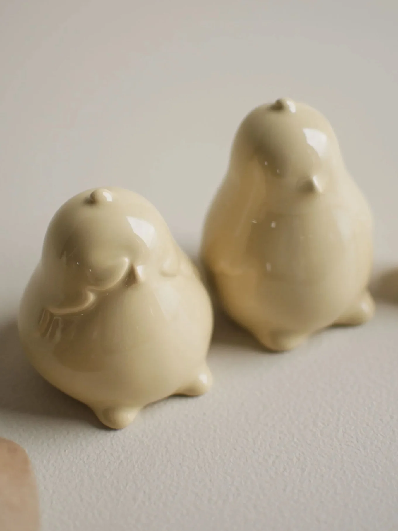 Two glossy, pale yellow ceramic bird figurines on a light surface.
