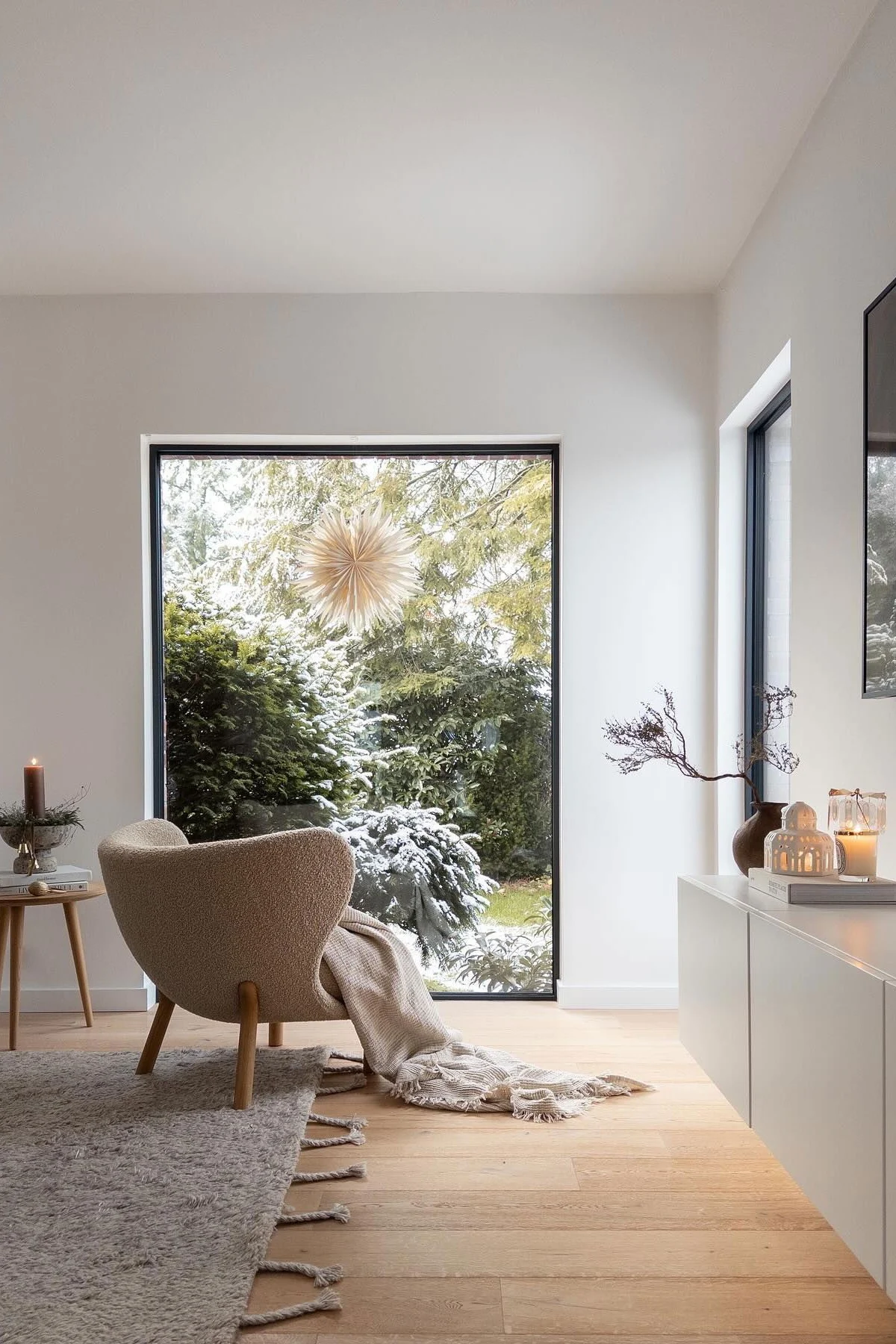 A living room with very minimalist Christmas decor. A Christmas star hangs in the window with a candle to the side. 