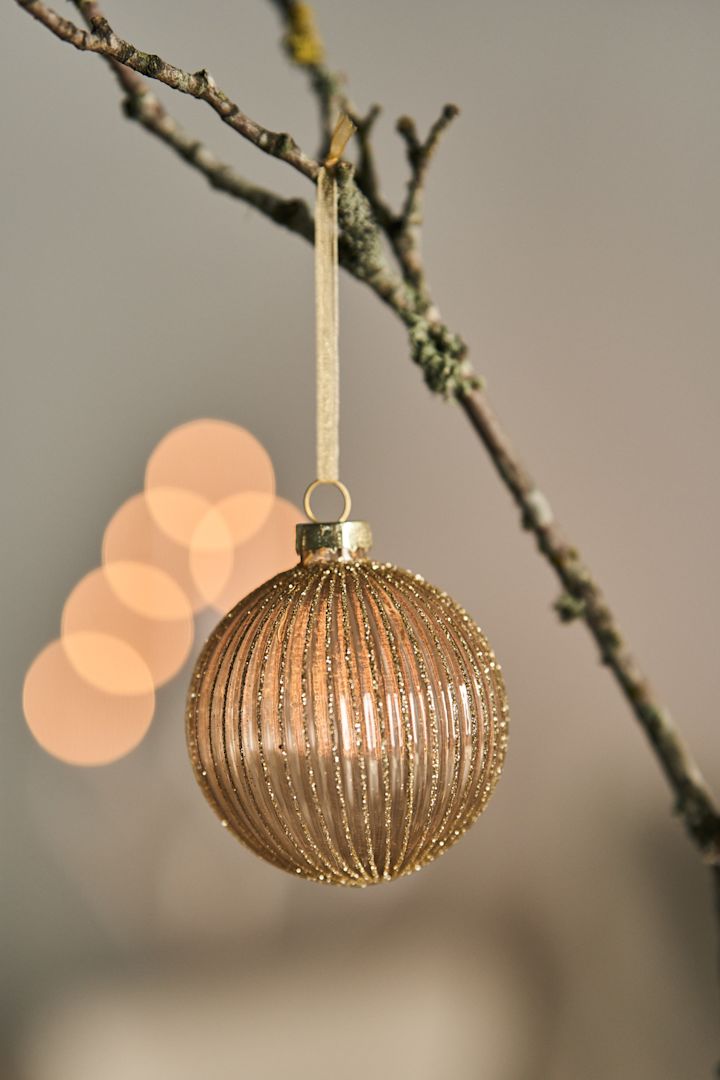 A minimalist Christmas bauble hanging on a branch with twinkling lights behind. 