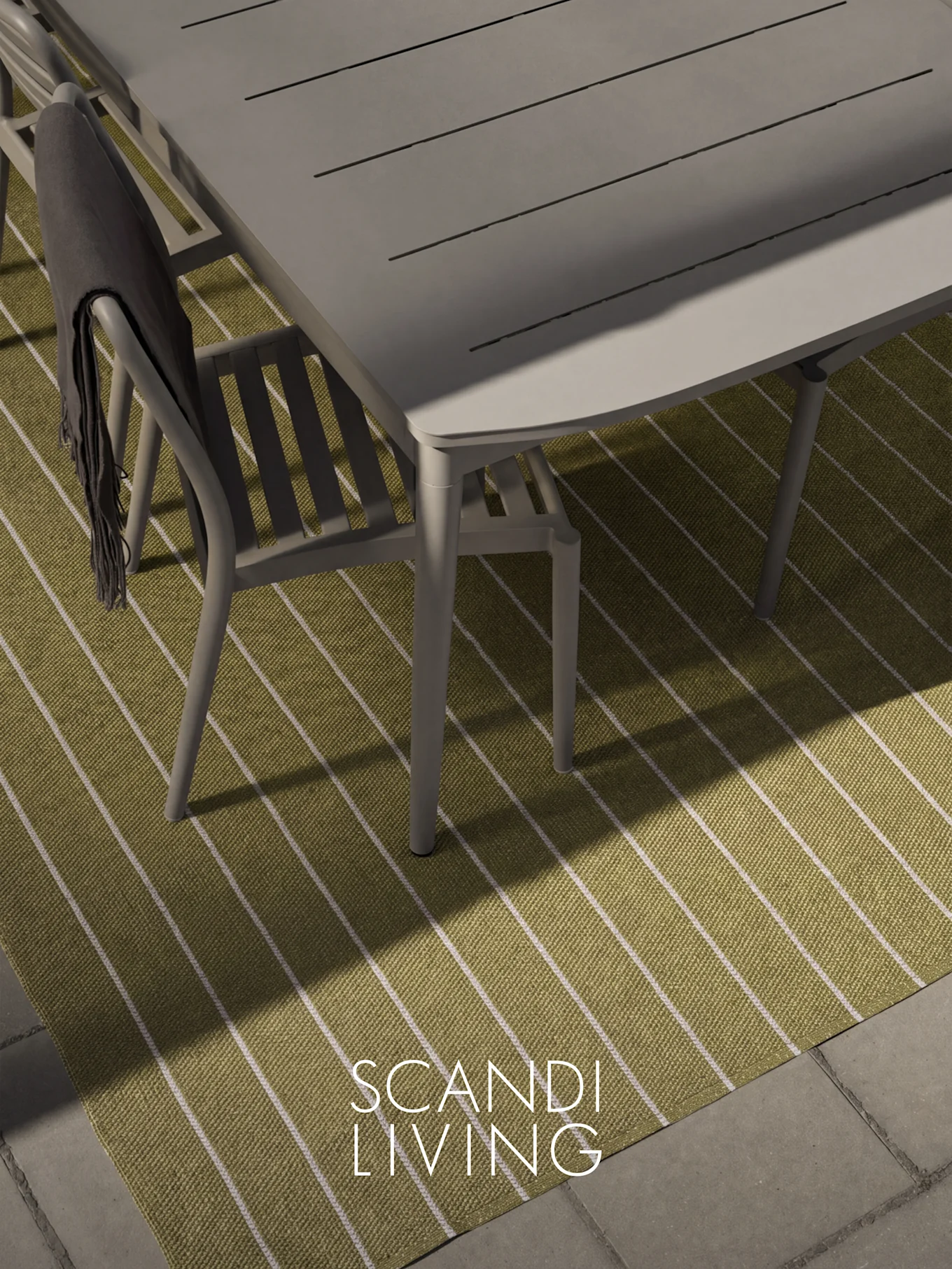 Overhead view of a gray outdoor dining table and chair with a dark throw on a green and white striped rug.