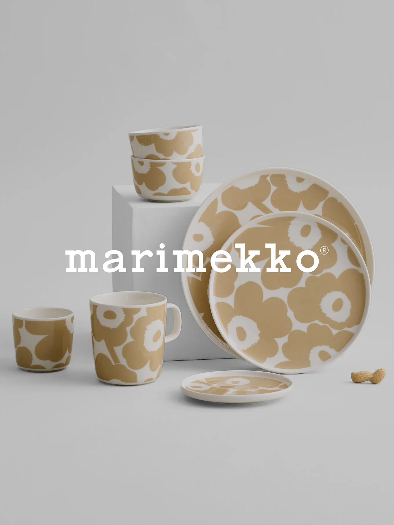 Marimekko dinnerware set featuring a beige and white floral pattern, with bowls, mug, cups, plates, and a peanut on a gray surface.