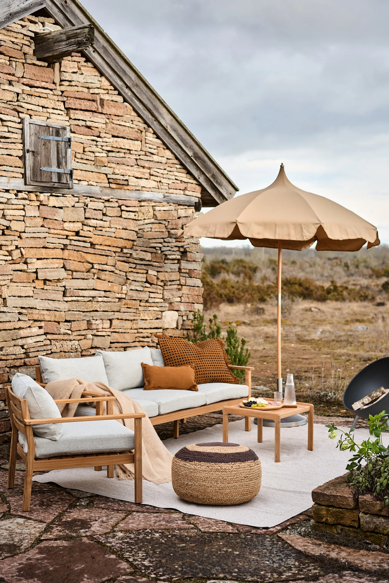 A seating area on a Mediterranean terrace with the beige Lull parasol from Ferm Living and the Melooni seat cushion from OYOY.