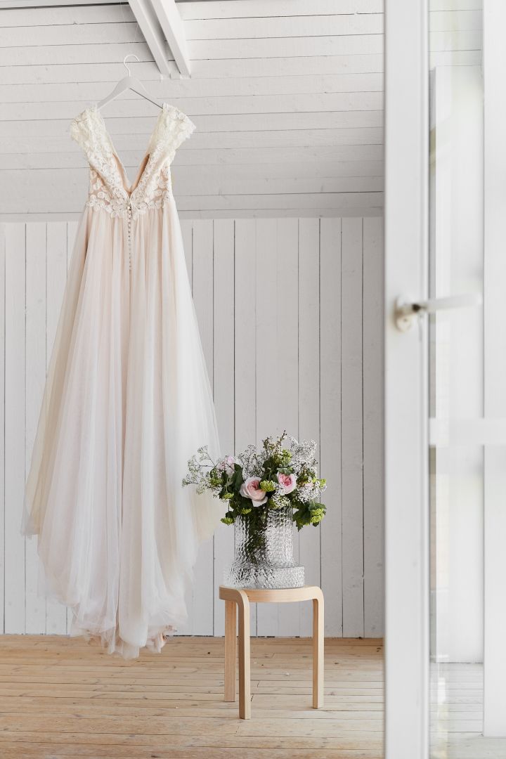 Unique wedding ideas need to be photographed to be remembered. Fill vases with beautiful flowers to enhance your photos, here you see a wedding dress hanging next to a wooden stool and a vase. 