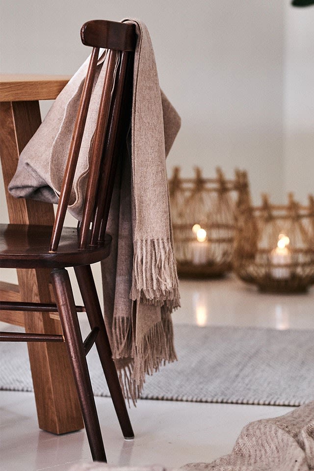 The beige Classic throw from Elvang Denmark hangs on a dining chair for an elegant and cosy dining area. 