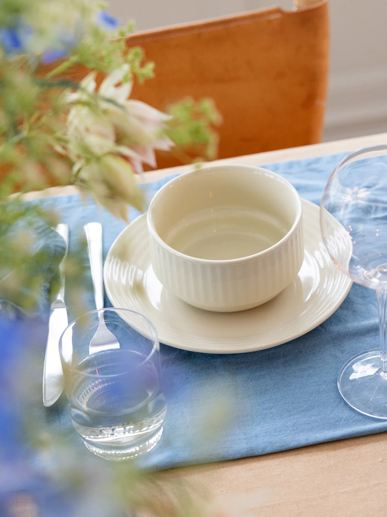 A table set with a light beige ribbed bowl and plate on a blue placemat, with cutlery and glasses.