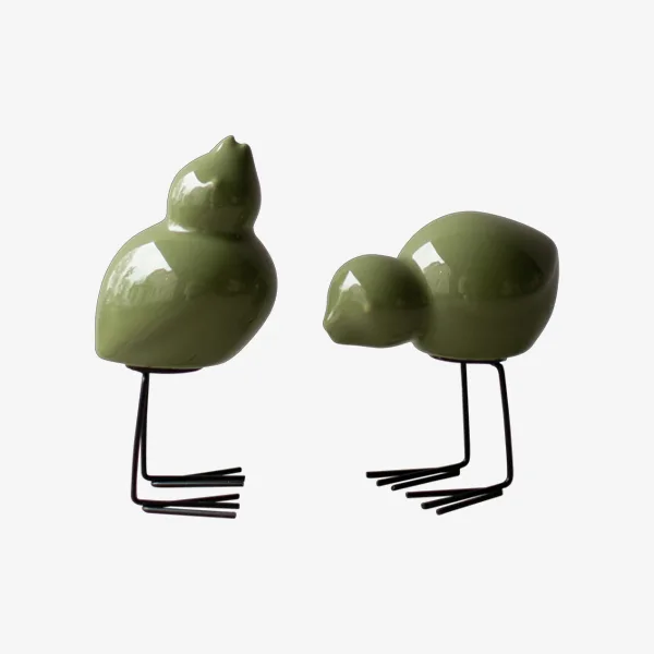 Two glossy green ceramic bird figurines with black wire legs, one standing upright, one bending down.