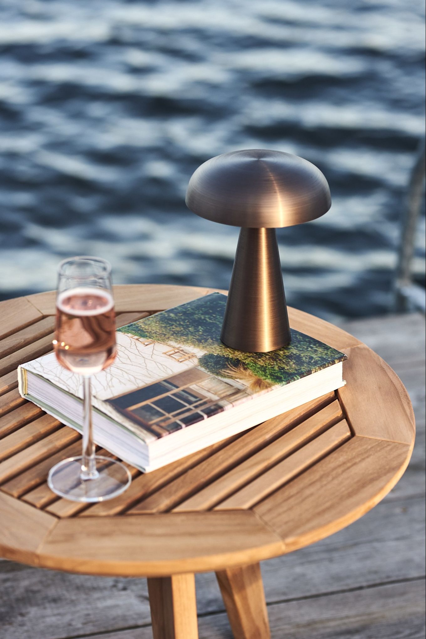 The cordless table lamp, Como from &Tradition seen here on a wooden table with a glass wine by the sea. 