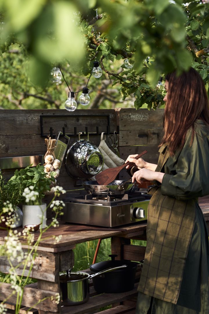 A woman cooks in the garden at her simple DIY outdoor kitchen made from pallets.
