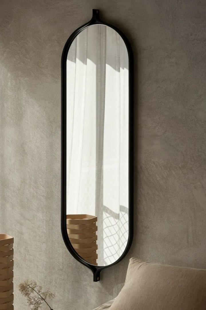 The Comma mirror in black ash hangs next to a bed from the Swedish furniture brand Swedese.