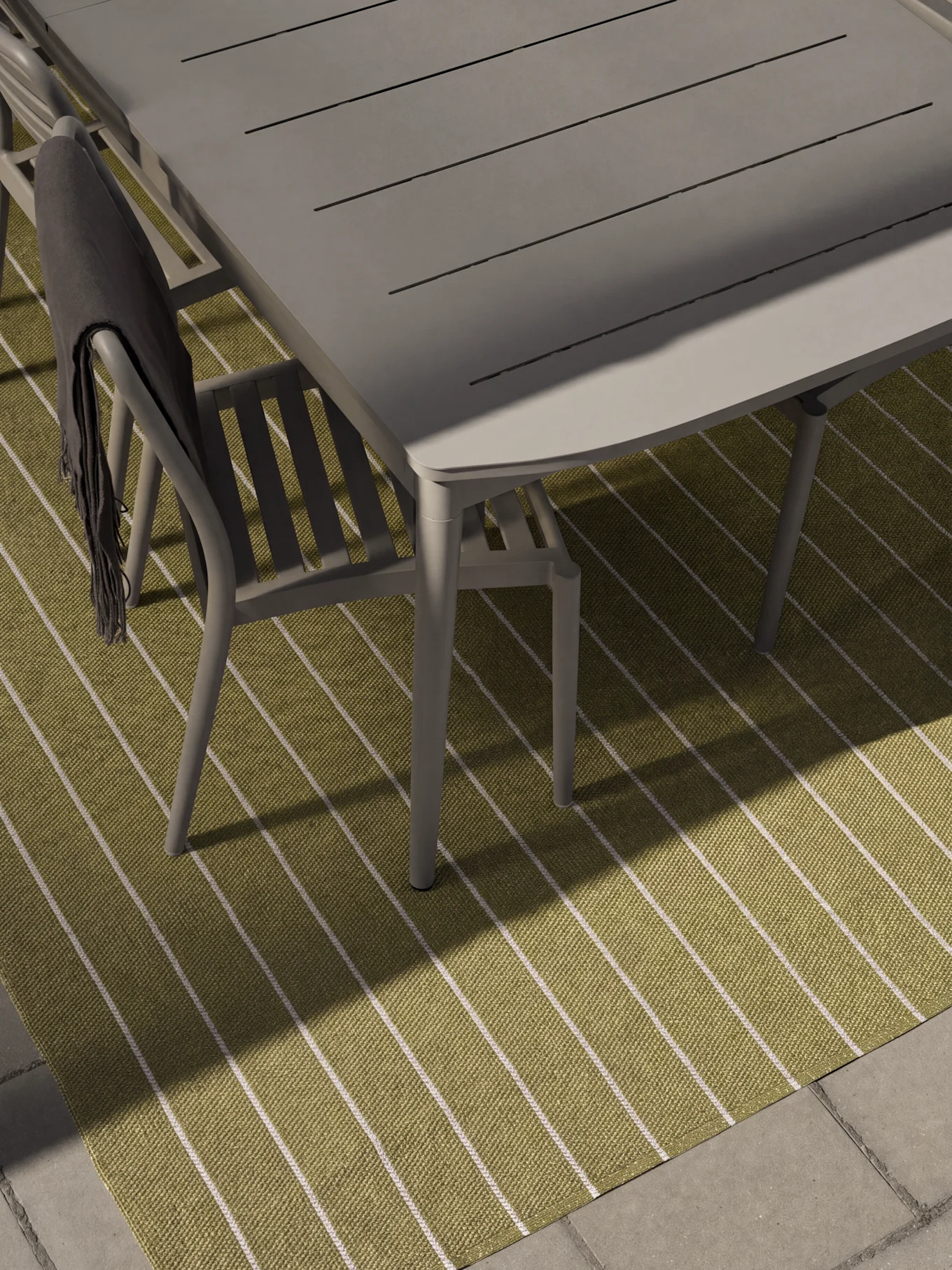 Grey outdoor dining table and chairs on a green and white striped rug. A dark grey blanket drapes over one chair.
